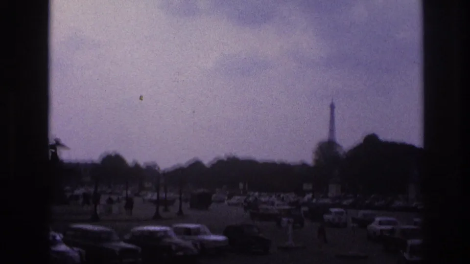 1967 Paris home-movie frame showing cars and small pedestrians around a broad circular roadway, with trees and the Eiffel Tower in the background.