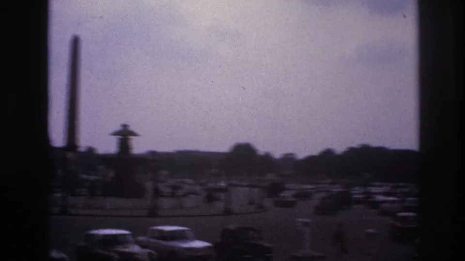 1967 Paris view across a busy circular roadway toward an obelisk and fountain, with cars, trees, and soft overcast light.