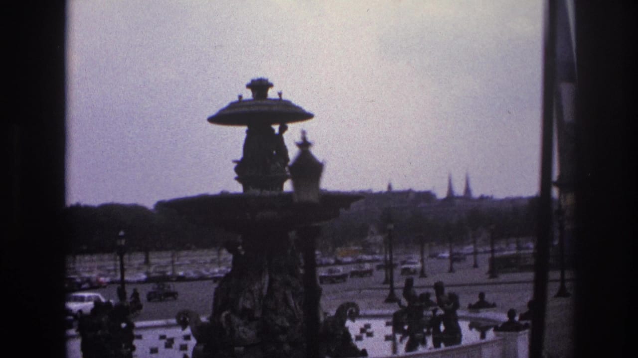 Fountain centered beside a traffic-filled square with pedestrians, lamps, and distant building silhouettes.