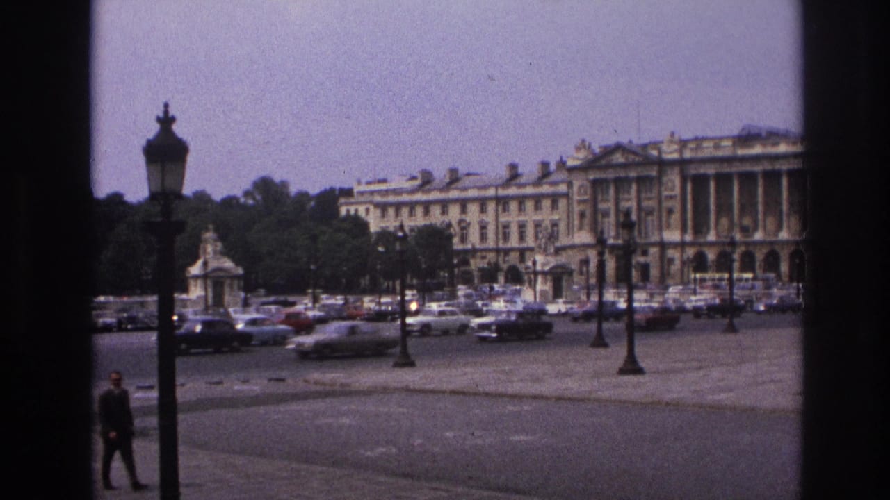 Public square with traffic, lampposts, trees, a stone building, and a pedestrian near the foreground.