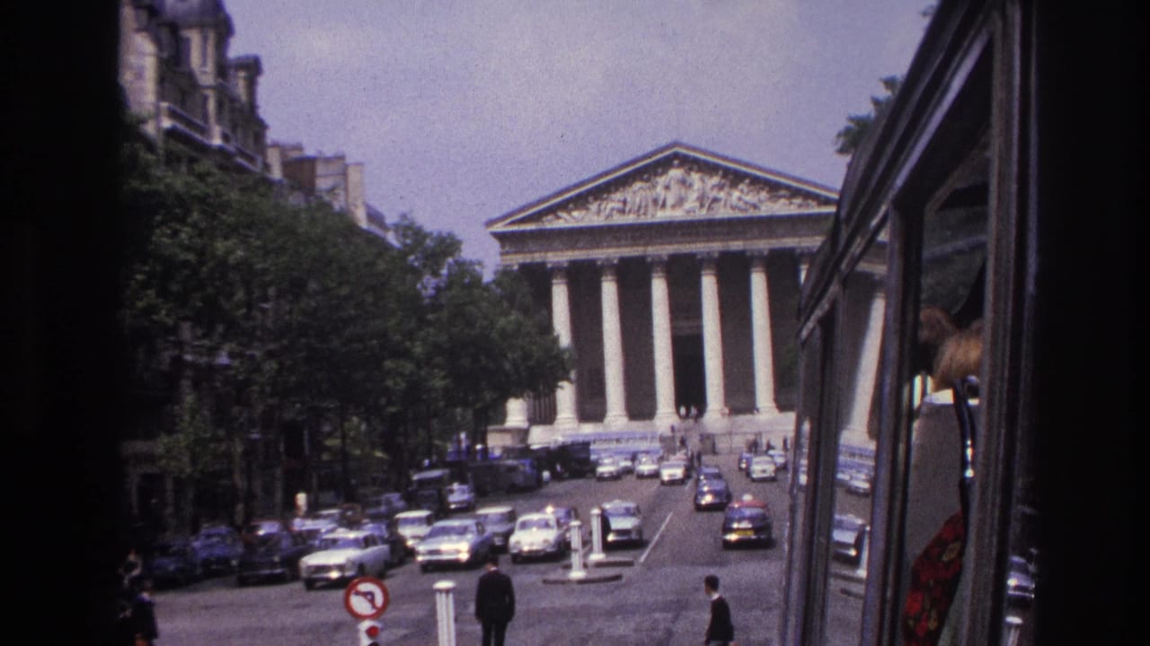1967 Paris view toward the Panthéon from a moving vehicle, with traffic, pedestrians, trees, and the vehicle edge at right.