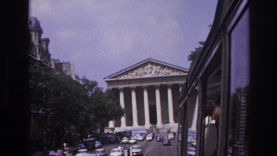 1967 Paris home-movie frame showing the Panthéon beyond moving traffic, trees, pedestrians, and a vehicle window edge.