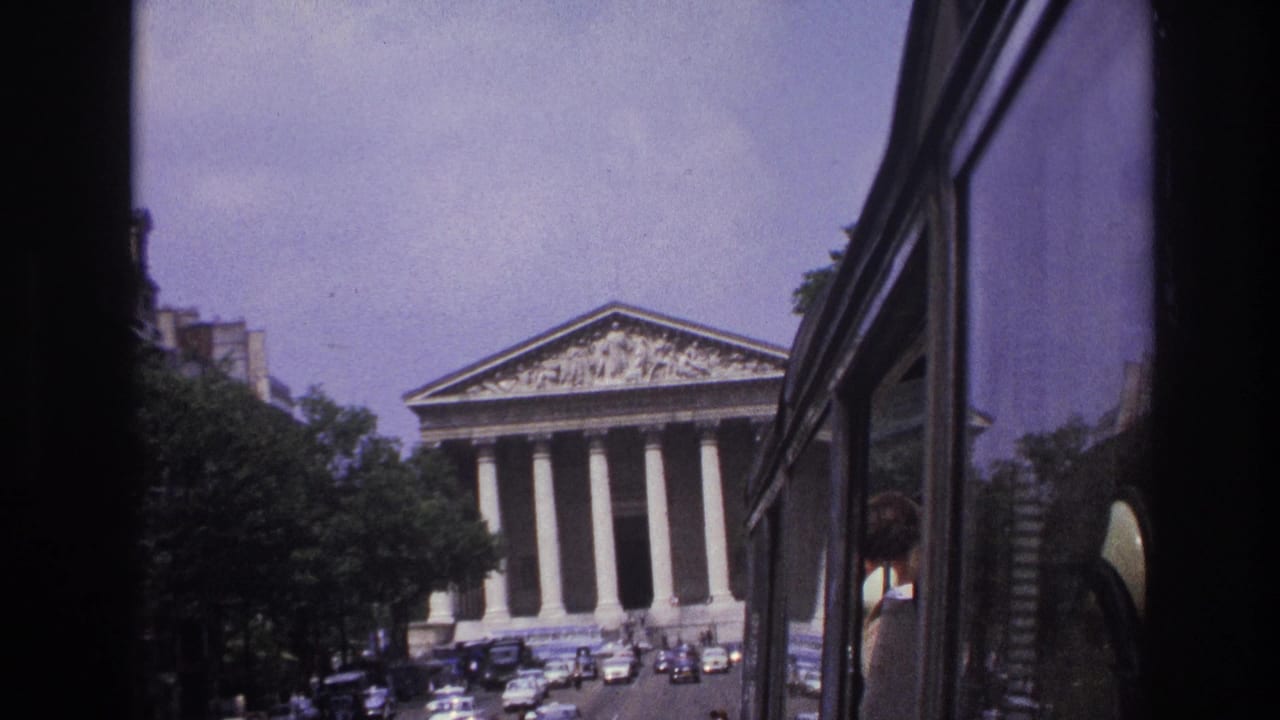 Neoclassical facade framed by a vehicle window with cars moving along the street.