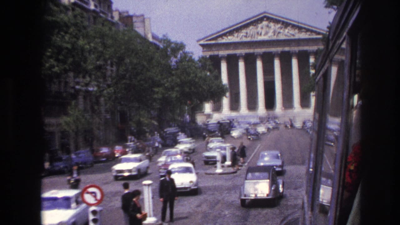 1967 Paris home-movie frame looking toward the Panthéon across a busy street with period cars and pedestrians.