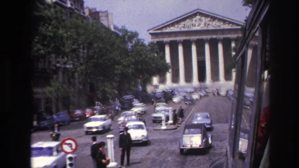 1967 Paris home-movie frame looking toward the Panthéon across a busy street with period cars and pedestrians.