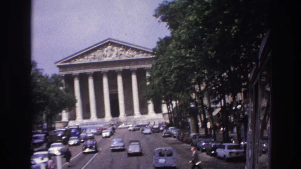 1967 Paris home-movie frame with a slightly tilted view of the Panthéon, street traffic, pedestrians, and parked cars.