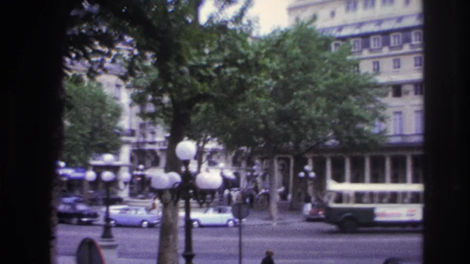 1967 Paris street view showing a green-and-white bus among classic cars, pedestrians, globe lamps, trees, and tall facade lines.