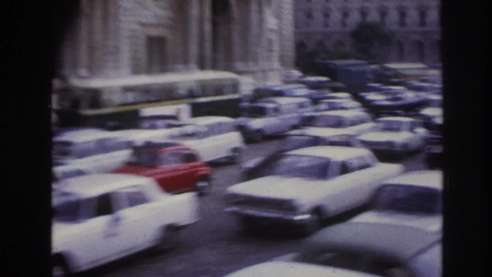 1967 Paris traffic view with rows of mid-century cars, a red car in motion, stone architecture, and soft 8mm blur.