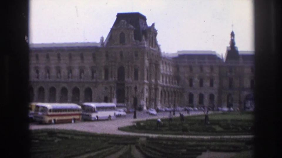 1967 Paris home-movie view of the Louvre exterior, tour buses, parked cars, garden paths, and dark vertical framing.