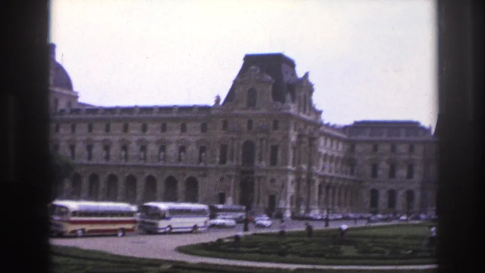 1967 Paris view across the Louvre grounds, showing tour buses, parked cars, formal lawns, and the museum facade.