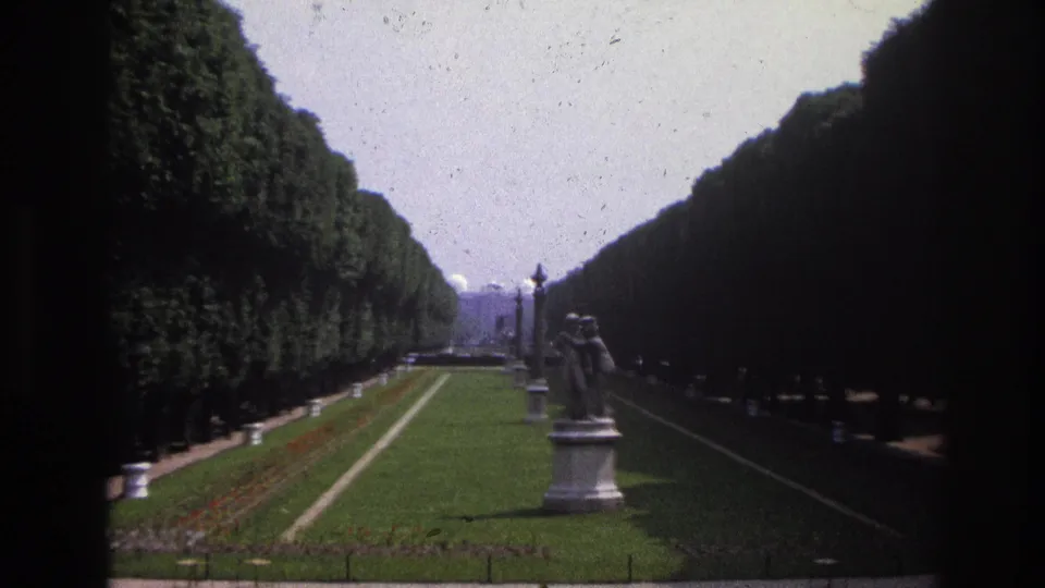 1967 Paris garden view near the Louvre, with manicured lawns, tree-lined paths, statues, and distant architectural forms.
