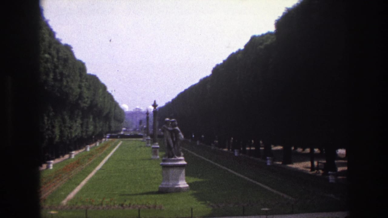 1967 Paris travel footage frames a formal garden aisle with dense clipped hedges, a green lawn, lampposts, and a classical statue.