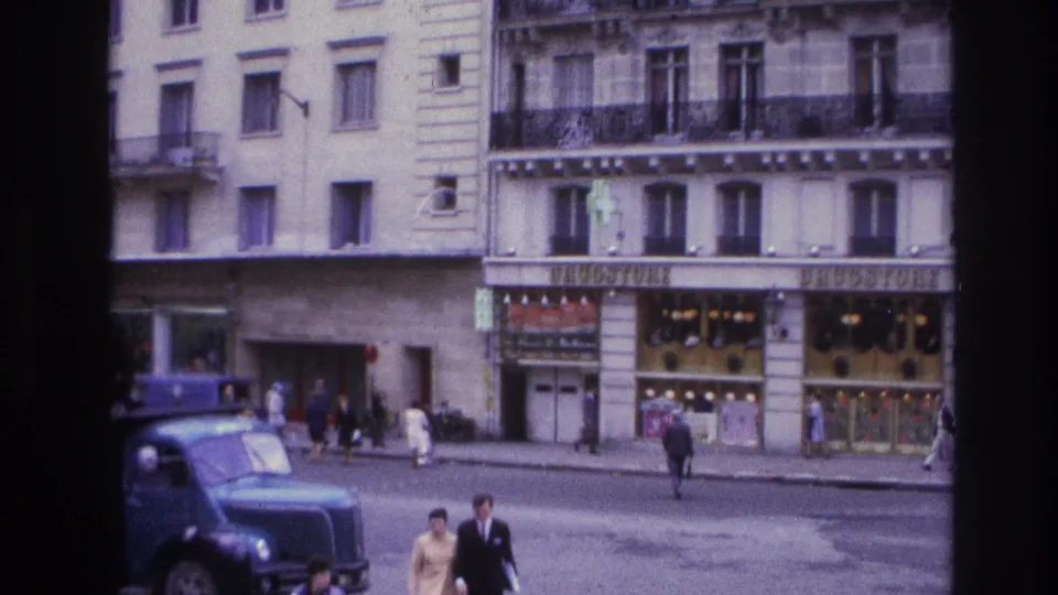 1967 Paris street cutaway with older buildings, shopfronts, pedestrians, and a blue truck parked or moving near the curb.