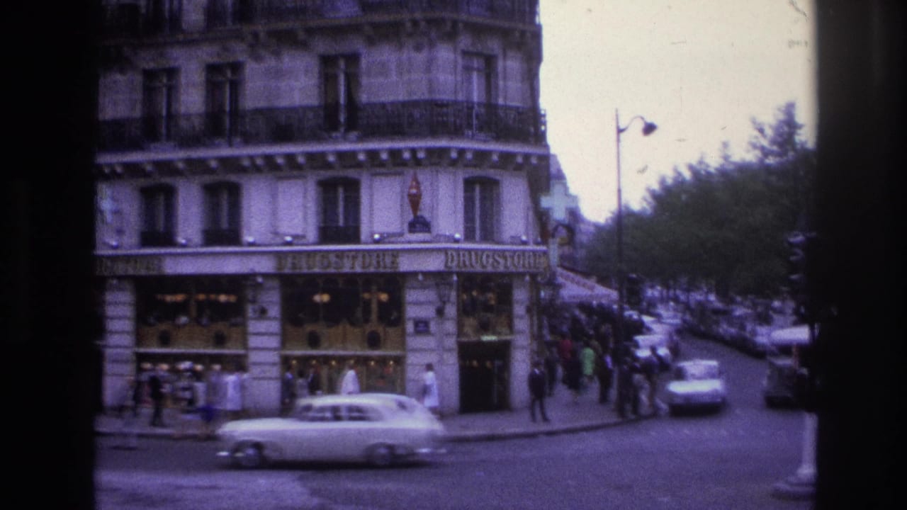 1967 Paris 8mm frame showing a corner drugstore building, pedestrians on the sidewalk, and white sedans moving through traffic.
