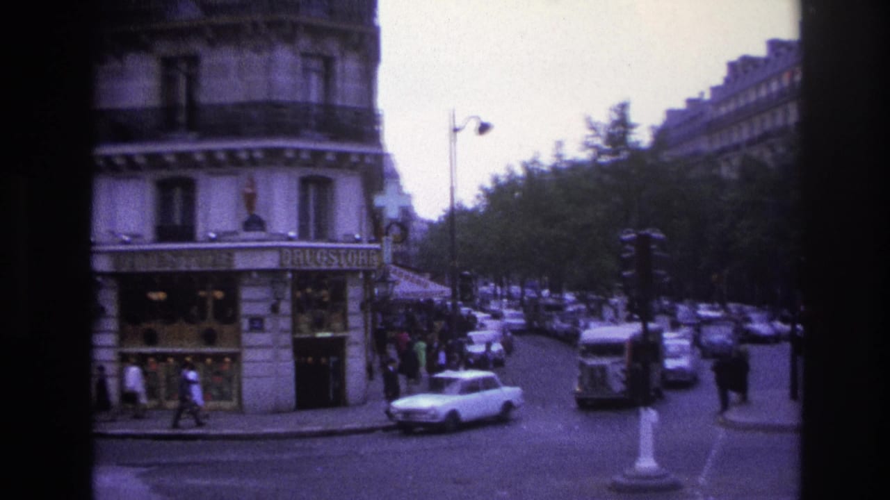 White car turns near a corner storefront while pedestrians and traffic fill the Paris street.