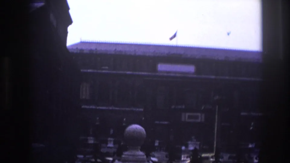 1967 Paris home-movie frame showing a dark foreground edge around a historic courtyard facade with a roof flag and stone ornament.