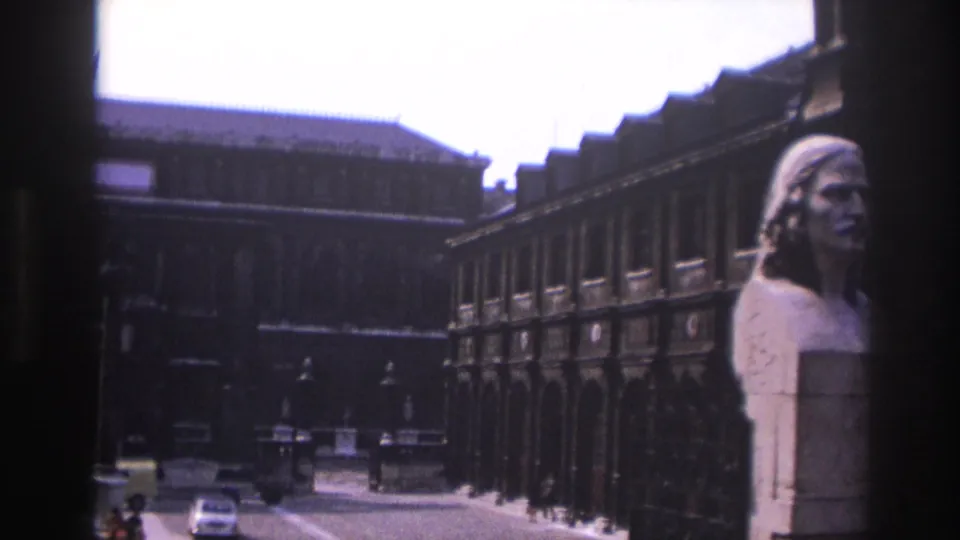 1967 8mm view of a Paris courtyard or street edge with a marble bust, ornate stone architecture, iron railing, and distant car.