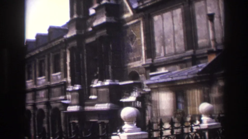 1967 Paris 8mm frame showing historic stone architecture, iron railings, lamps, and courtyard details as the camera pans away from the bust.