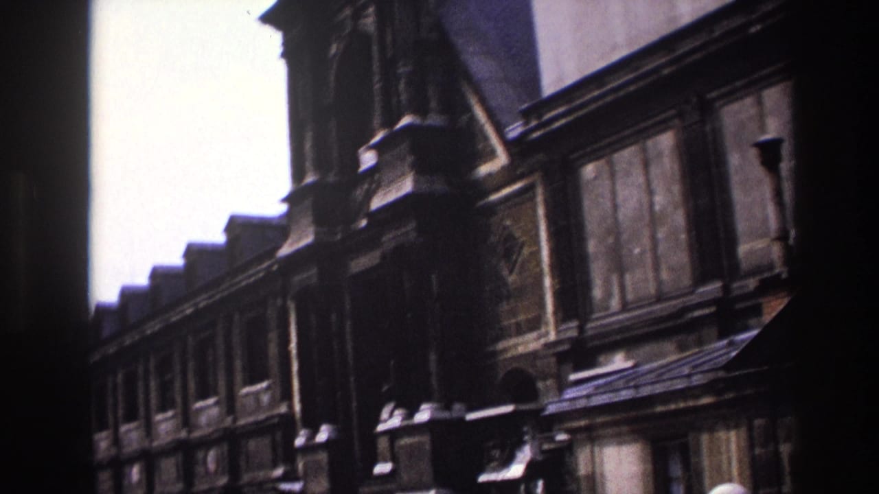 1967 Paris home-movie frame showing a low-angle view of an ornate dark stone facade, upper windows, and roofline against a pale sky.