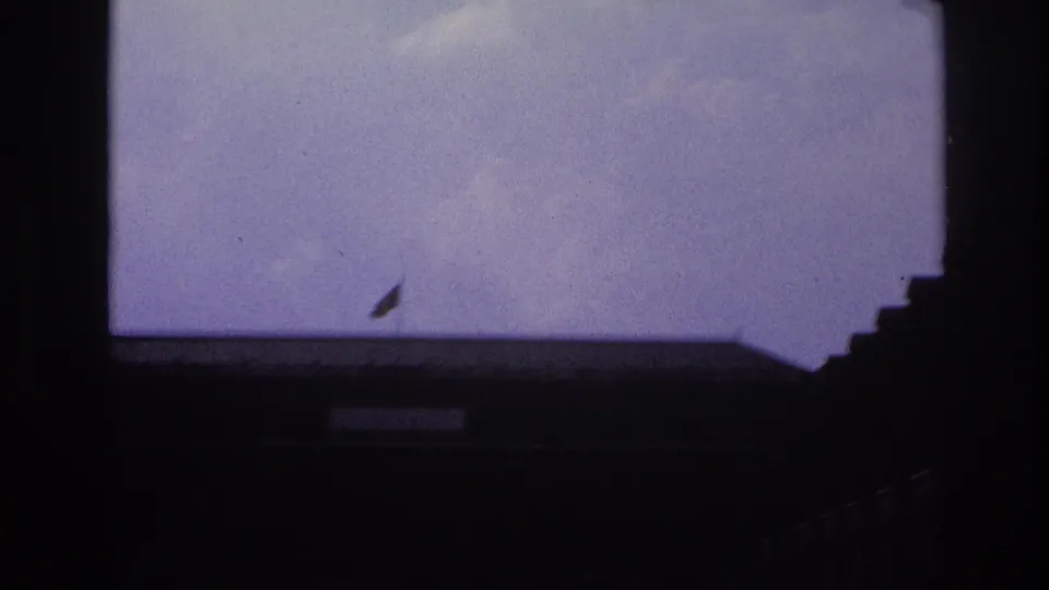 1967 Paris frame showing a dark roofline or courtyard edge in silhouette, pale sky, and a small flag at the left side.