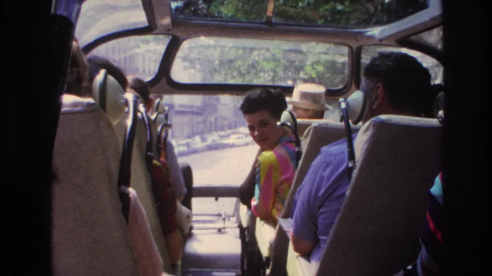 Open-top Paris sightseeing bus interior with seated passengers, curved windows, and a rider glancing toward the camera.