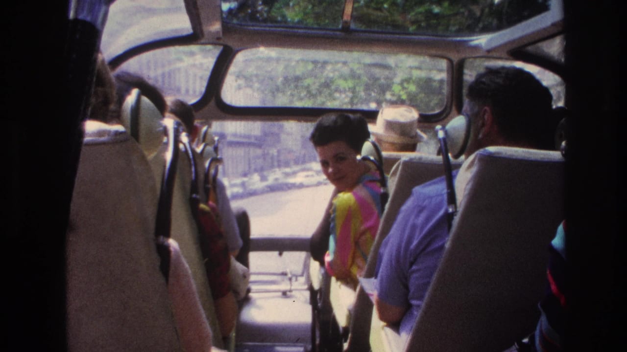 1967 Paris home-movie frame showing adults seated inside a sightseeing bus, including a woman in a colorful striped top.