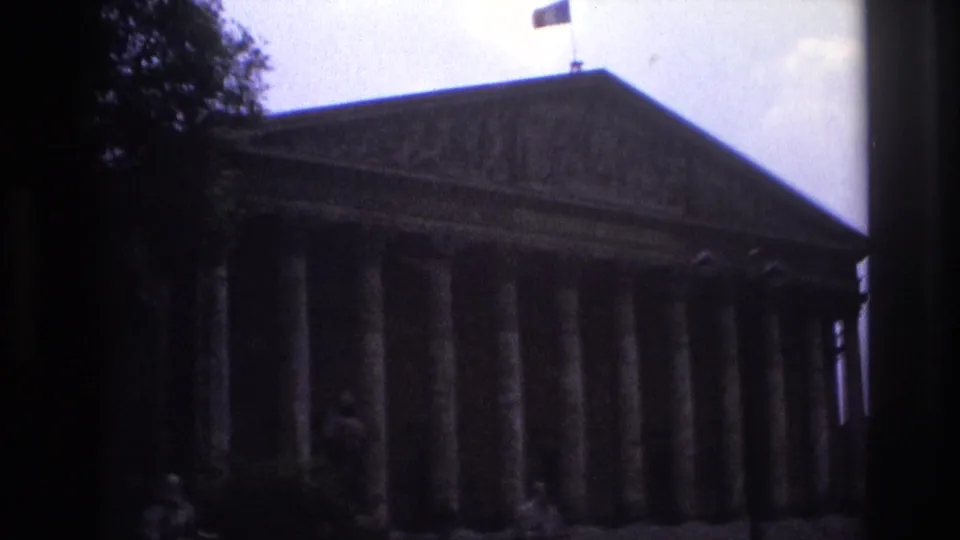Paris travel footage shows a shadowed classical facade with columns and a flag, filmed from a moving vehicle.