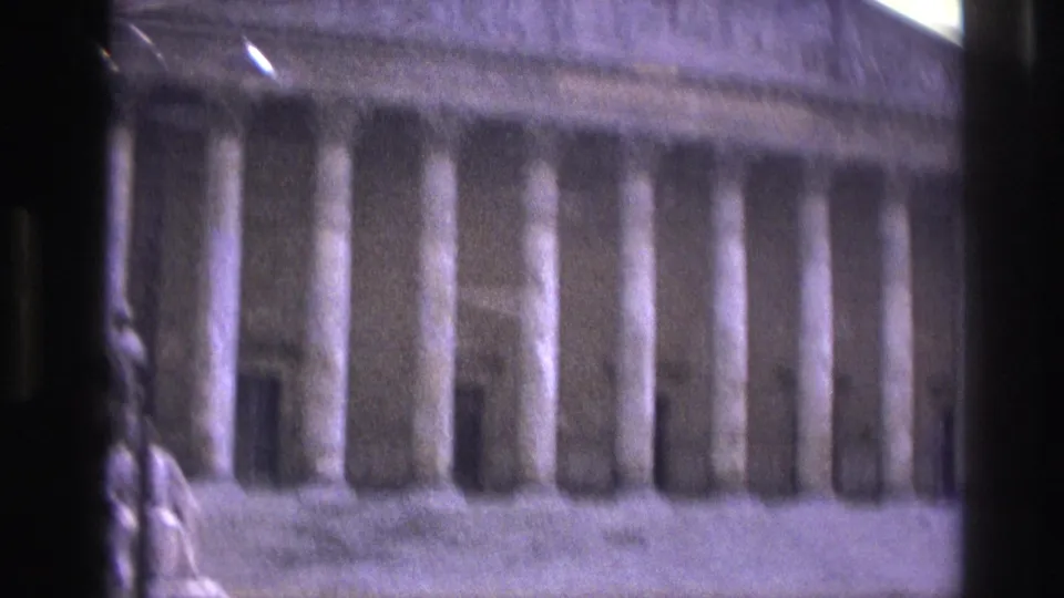 Soft, grainy 8mm frame of a Paris columned landmark facade, seen close from a moving sightseeing vehicle.