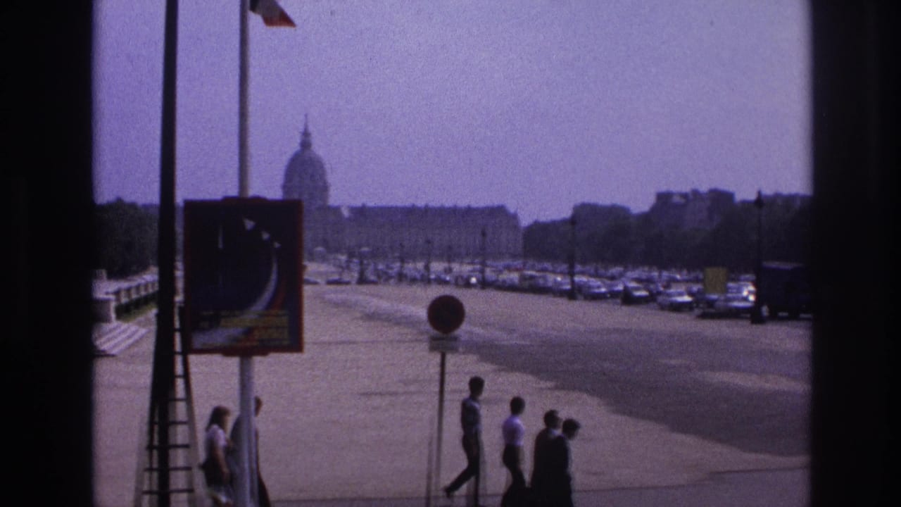 1967 Paris street view through a window, with pedestrians, a traffic sign, parked cars, and a distant domed building visible in haze.