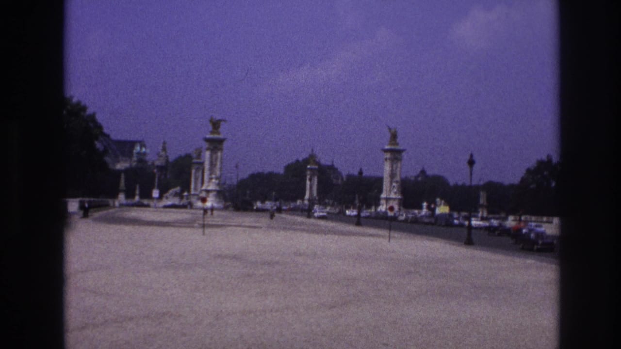Bridge roadway with tall decorative pylons, distant pedestrians, cars, and lampposts.