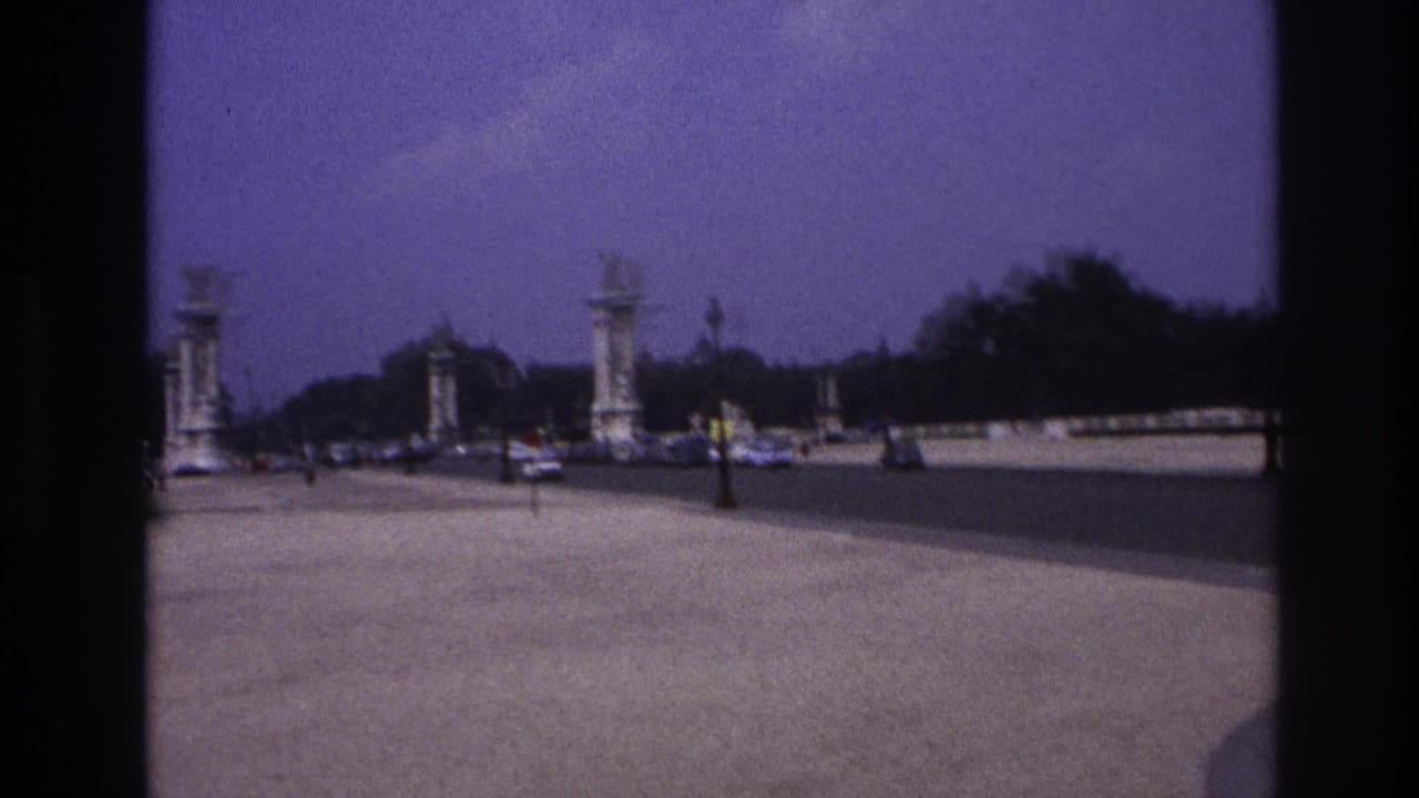 1967 Paris home-movie view of Pont Alexandre III from behind a dark window frame, with period cars and bridge lamps ahead.