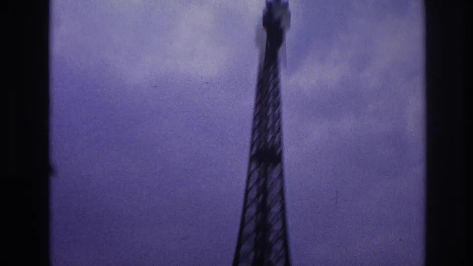 1967 Paris home-movie shot looking up at the Eiffel Tower against a purple-tinged sky with soft 8mm focus.