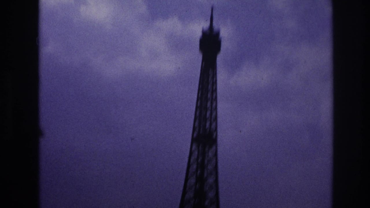 1967 Paris home-movie frame showing the upper Eiffel Tower in silhouette beneath a cloudy, purple-shifted sky.