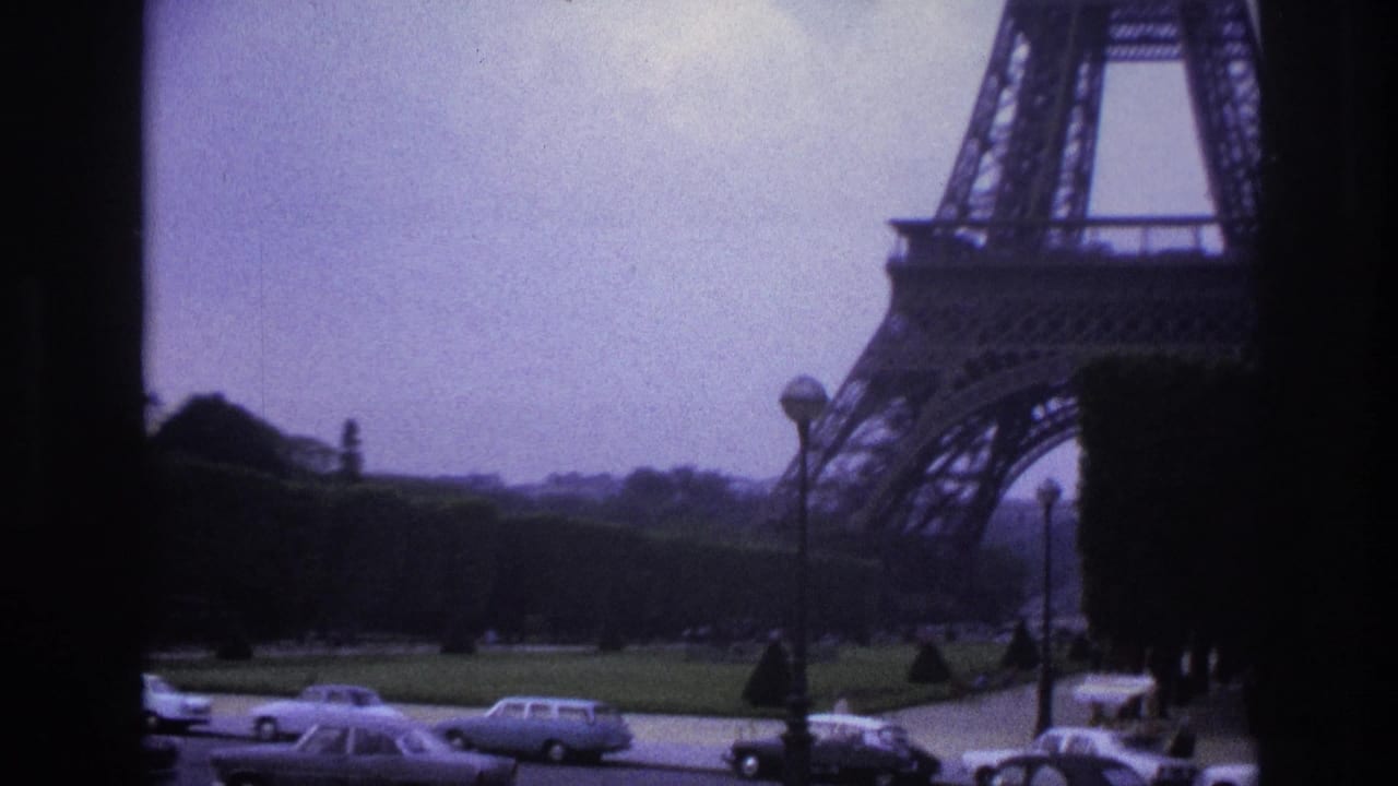 Eiffel Tower base beside lawns and a road with vintage cars, seen through dark window framing.