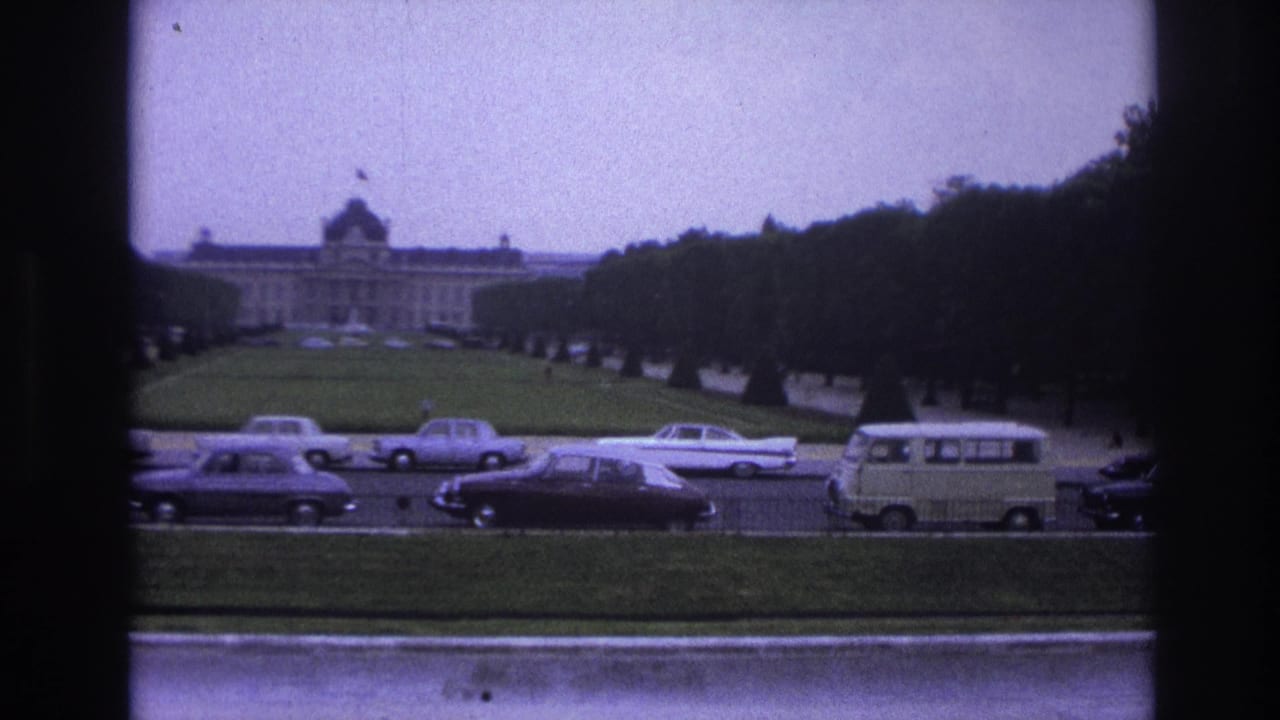 1967 Paris home-movie view of a formal lawn, distant classical building, and mid-century cars passing along the road.