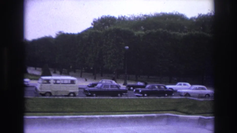 1967 Paris traffic cutaway with mid-century cars, a light van, formal grass, and trees under an overcast sky.