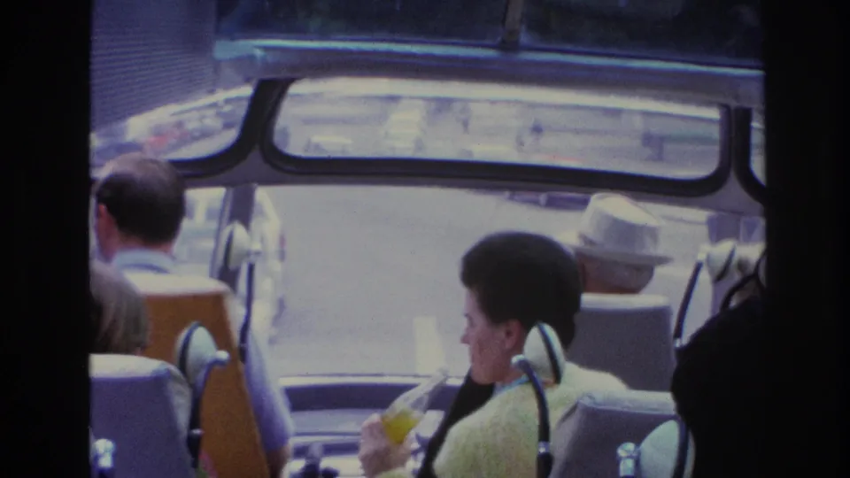 1967 Paris home-movie view from inside a bus, showing tourists, seat hardware, and the street ahead through soft 8mm exposure.