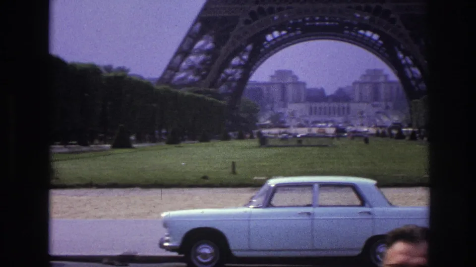 Paris Eiffel Tower view from across the lawn, with a pale vintage car partly crossing the lower frame.