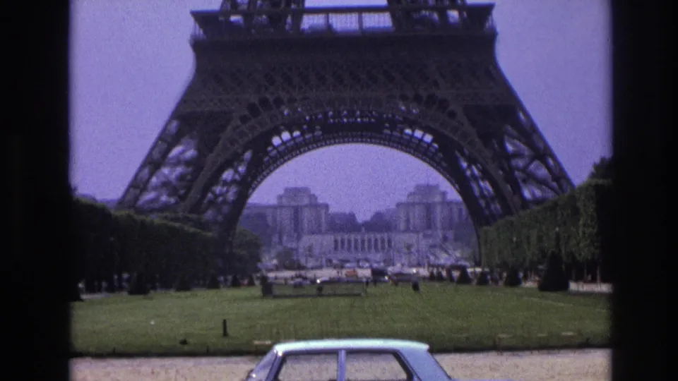 Eiffel Tower rising over Champ de Mars lawns in 1967 Paris footage, with a pale sedan at the lower edge.