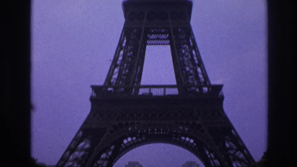 Closer 1967 Paris view of the Eiffel Tower lower span and latticework, partly bounded by dark vertical frame edges against a grey-blue sky.