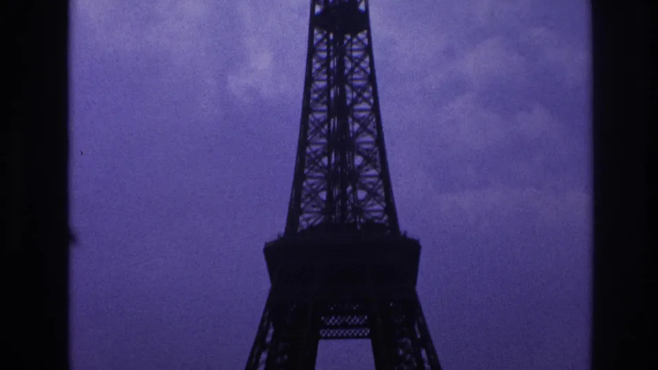 1967 Paris view of the Eiffel Tower upper structure, cropped by dark frame edges and set against a cloudy purple-blue sky.