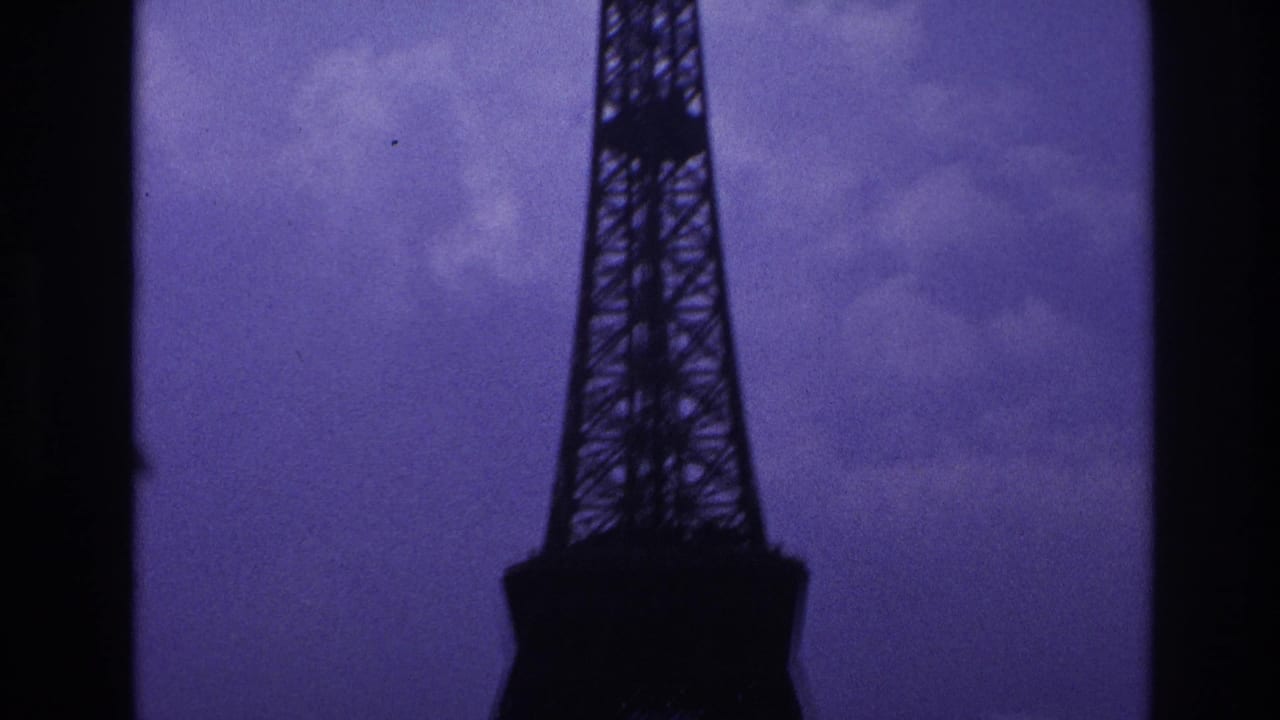 1967 Paris 8mm frame with the Eiffel Tower lower section silhouetted against an overcast purple-blue sky.