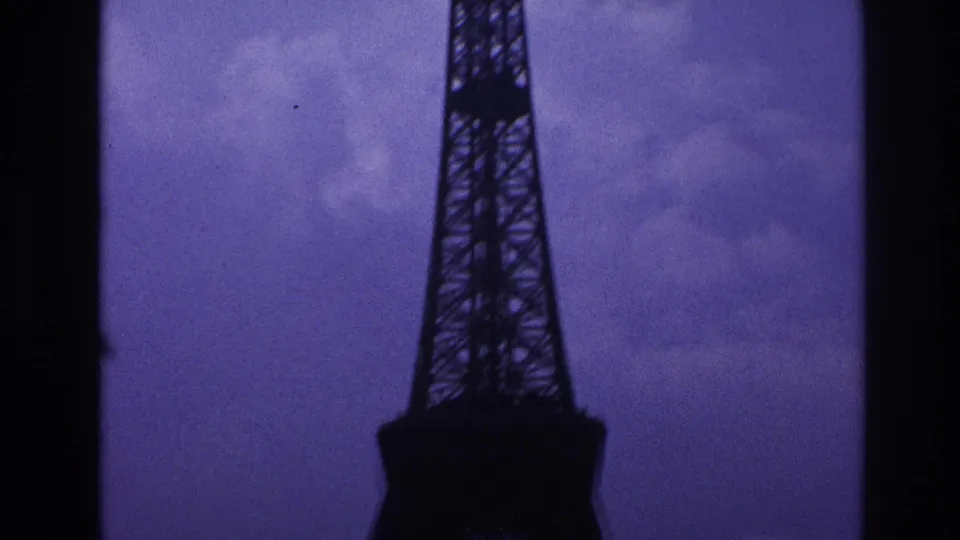 1967 Paris 8mm frame with the Eiffel Tower lower section silhouetted against an overcast purple-blue sky.