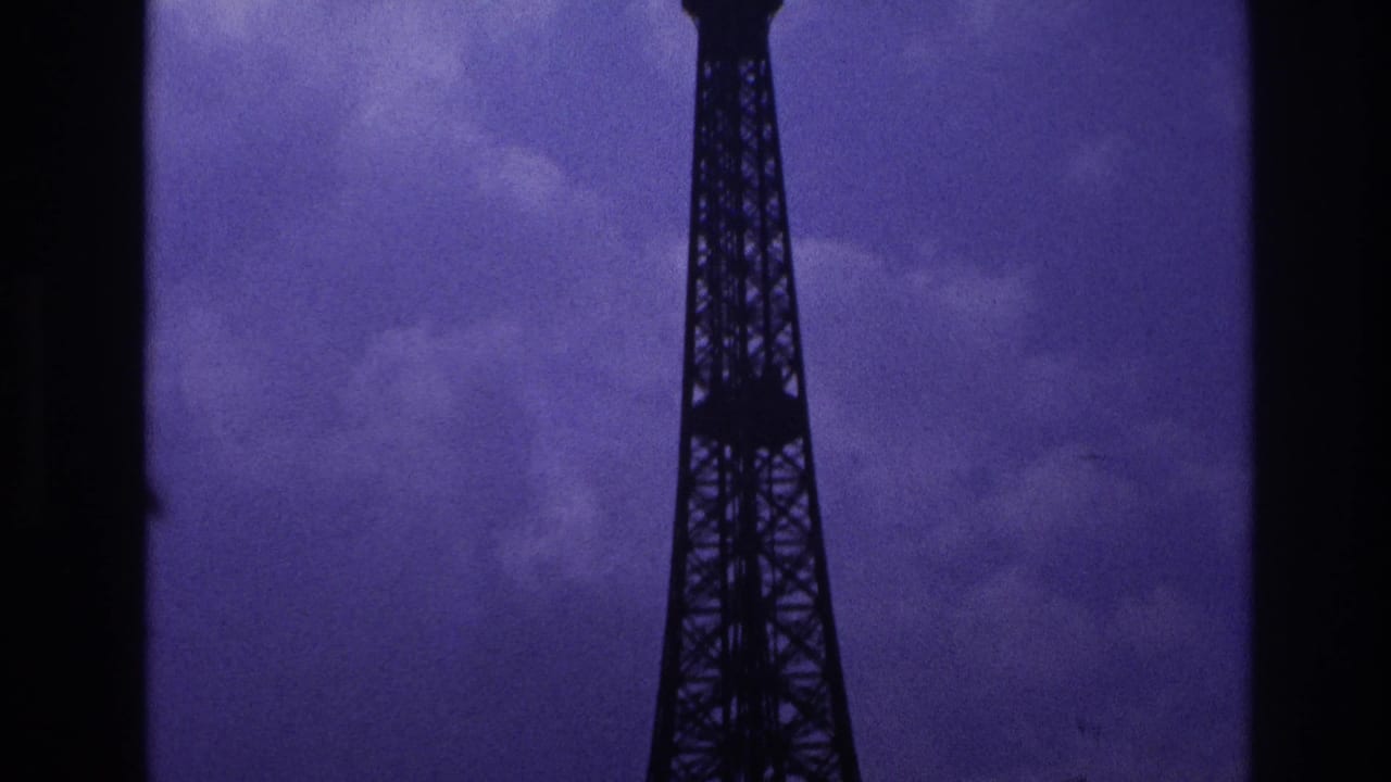 1967 Paris 8mm frame showing the upper Eiffel Tower silhouetted against grey-purple clouds with a dark film edge nearby.