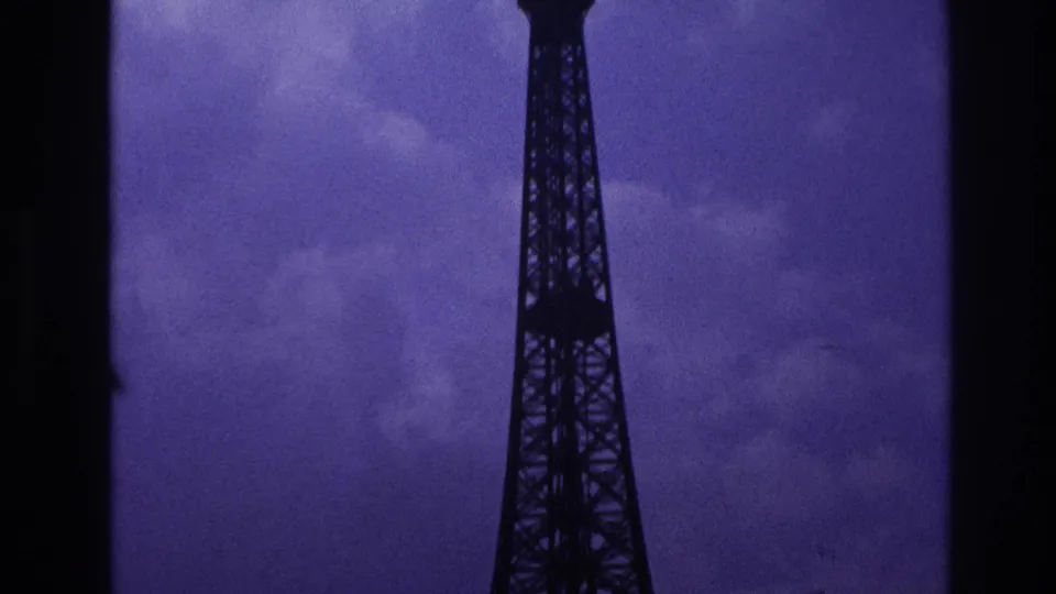 1967 Paris 8mm frame showing the upper Eiffel Tower silhouetted against grey-purple clouds with a dark film edge nearby.