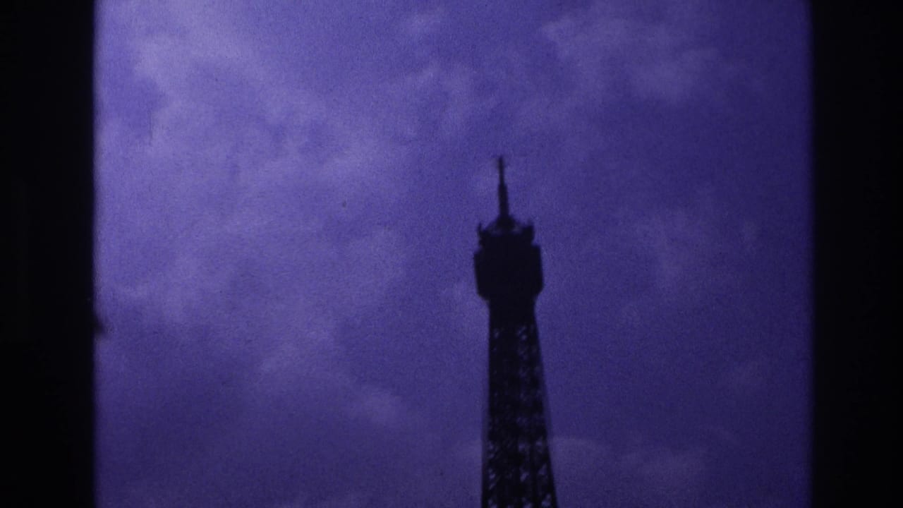 1967 Paris 8mm frame showing the upper Eiffel Tower in silhouette beneath a dark purple clouded sky.