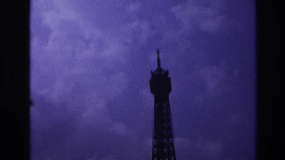 1967 Paris 8mm frame showing the upper Eiffel Tower in silhouette beneath a dark purple clouded sky.