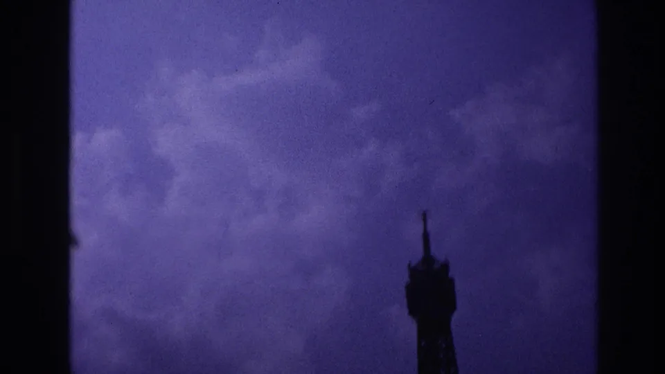 1967 Paris 8mm still with the Eiffel Tower upper section silhouetted from below against a textured purple sky.