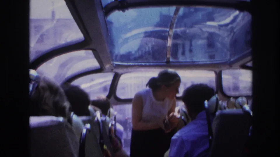 1967 Paris transit interior showing a woman leaning toward a passenger, with roof glazing, seat rows, and bright exterior light visible.