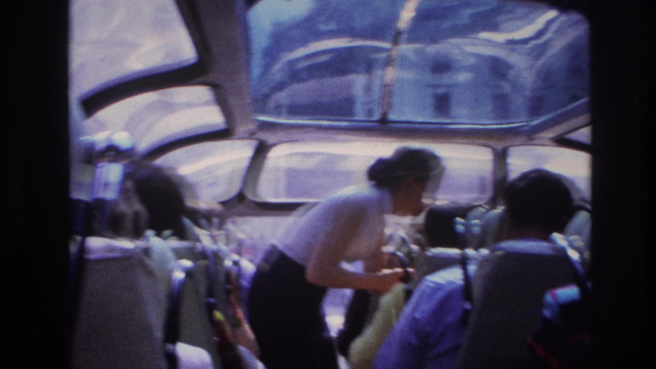 1967 Paris tour bus interior with seated passengers, curved windows, and a woman in a white top bending to speak with someone nearby.